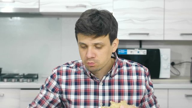 Tired young man in a plaid shirt eats a big cheburek with an appetite and drinks.