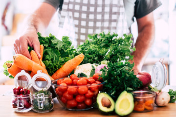 Man preparing vegetarian and vegan food - table full of fresh seasonal healthy vegetables - mix of colors and vitamin - focus on hand taking a carrot - wellnesss lifestyle concept