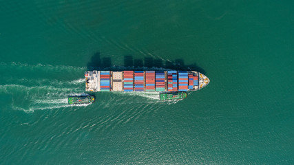 Aerial top view container ship and tug boat going to sea port for logistic, import export, shipping or transportation.