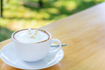 White cup of coffee latte with cute cat shape latte art milk foam on wood table.