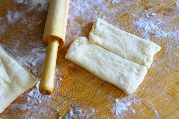Dough, flour and rolling pin on a wooden board. Cooking buns with sugar and poppy seeds. Close-up. Background.