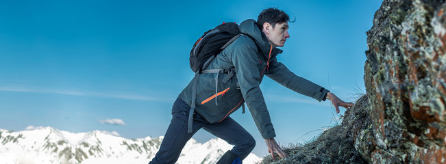 Tourist with a backpack crawling on rocks to the top on the background of mountains. Motivation and goal achievement