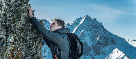 Tourist with a backpack crawling on rocks to the top on the background of mountains. Motivation and goal achievement