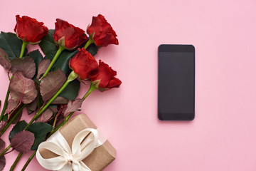 Obraz na płótnie Canvas Day to celebrate their love. Top view of fresh red roses, gift box and black cellphone