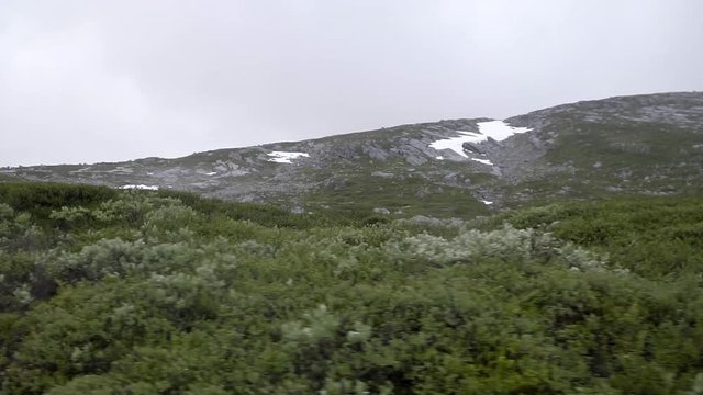 Driving through the Old Strynefjell Mountain Road in Norway with bad weather conditions and mountains with snow in the background in slow motion.