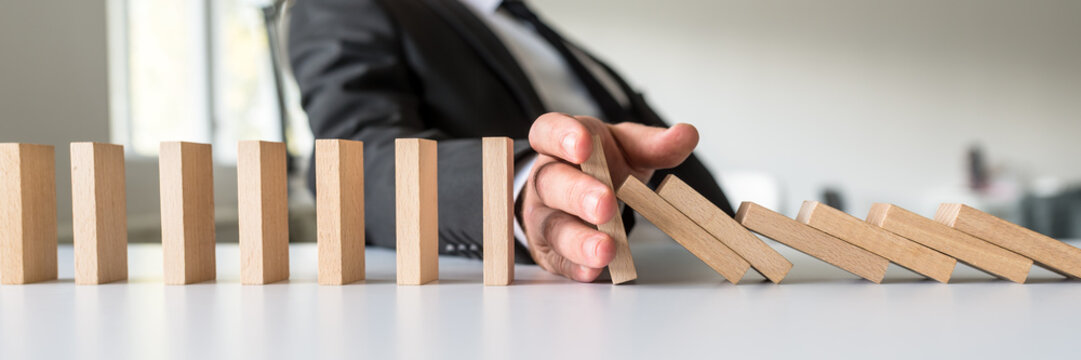 Business mediator stopping falling wooden dominos with his hand
