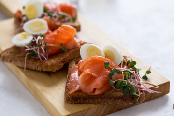 Toasts with smoked salmon garnished with quail egg and radish sprouts
