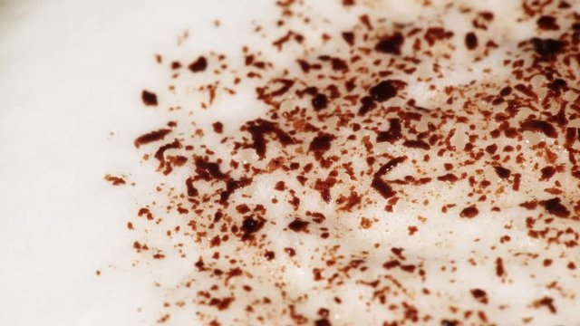 Close up of hot coffee cup with frothed milk foam and chocolate shavings decoration as rotating fod background