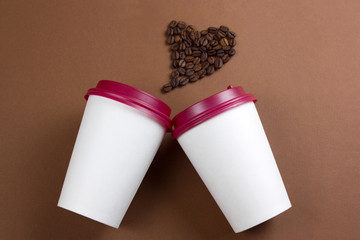 top view white paper coffee to go cups and heart made from coffee beans, white mock up paper cups, copy space, brown background