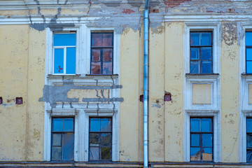 The facade of an old abandoned building with peeling paint, broken windows and a drainpipe