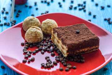 Tiramisu cake on a red plate, near a cup of coffee, photographed on a light wooden background.