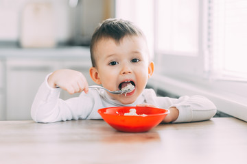 A child in the kitchen eating their own oatmeal with a red plate