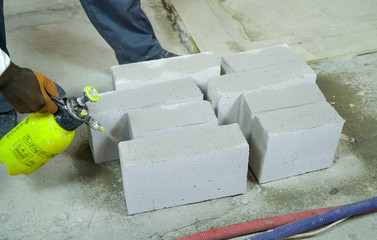 construction worker moisturing aerated concrete blocks with water sprayer
