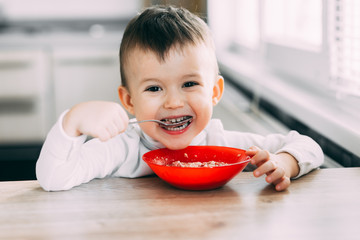 A child in the kitchen eating their own oatmeal with a red plate