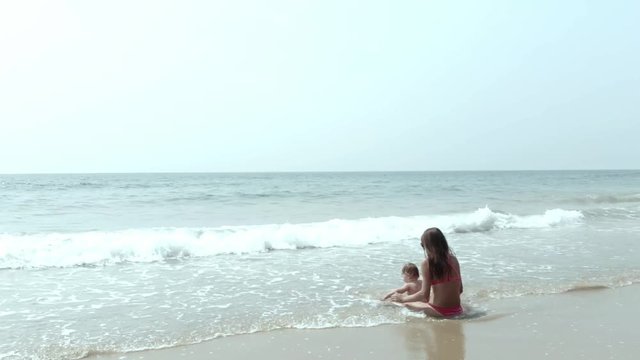 Mom and girl playing on the beach of the sae sit, walk and swim. Mom and daughter are sitting in the sea and watching the waves.