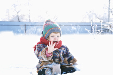 baby in winter clothes outdoor remove her mittens and say hello. cute child in cap,scarf and mittens among the snow