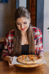 Beautiful and sexy girl sitting by the window in a cafe and holding a pizza.
