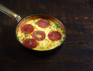 fried omelet with sausage in a pan on a wooden background. rustic style.
