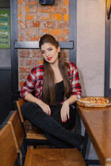 Beautiful and sexy girl sitting at a table with a pizza in a cafe.