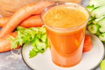 Fresh green celery, juice in glass on background near the carrots. 