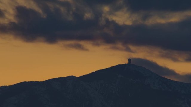 Orange sunset clouds behing a snowed mountain
