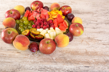 Fruit mix. Peach, grapes, apple, watermelon, cantaloupe, raspberry, plum. Whole fruits and slices on a plate lie on a white wooden background. Copy space, Place for text. 
