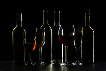 Bottles of wine and different glasses of wine on a dark background