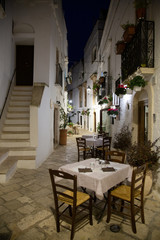 Narrow white street and restaurant in Locorotondo at night, province Bari, Italy