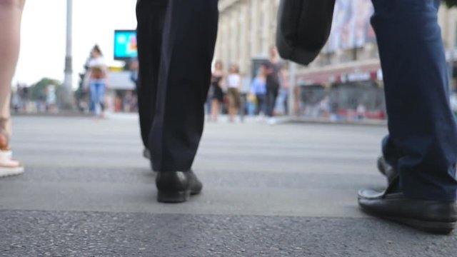 Feet of two businessmen crossing road in downtown. Legs of male coworkers walking a crosswalk in big city. Young colleagues commuting to work together. Blurred motion. Rear view Slow motion Close up