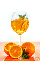 orange cocktail in wine glass with mint on white background with oranges