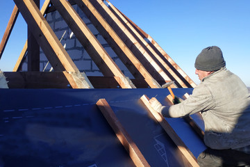 The master nails the bars, fixing this gidrorizer to the rafter, the blue sky appears on the background