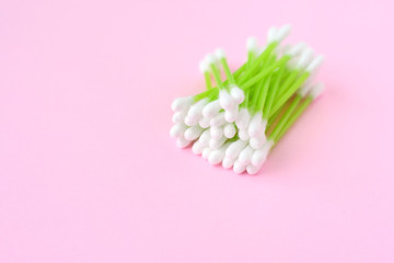 Individual ear sticks with green plastic pick and cotton buds with selective focus on pink background. Clean ear swabs for personal ears hygiene. Sterile softness applicator for cleanliness earwax 