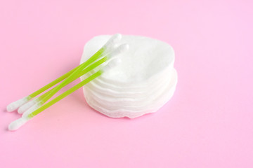 Clean cotton stack of disk for beauty hygiene with selective focus and individual ear sticks with sterile softness applicator on pink neutral background. Ear swabs and face sponges for health