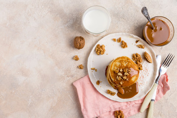 Free space with stack of pancakes with caramel and nuts at white plate on white background