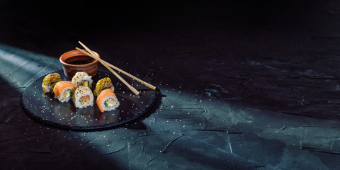 A different assortment of sushi rolls on a black coal board and a dark background. Traditional...