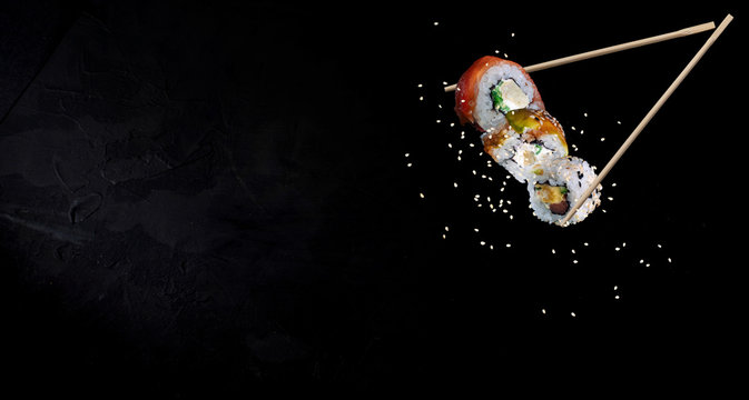 Sushi pieces placed between chopsticks, separated on black background. Traditional japanese food
