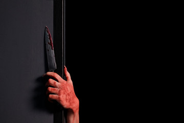 A woman's bloodied hand stuck a knife out from behind a wall. Black background. Concept of celebrating Halloween, horror and fear. Close-up. Copy space.