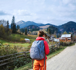 Naklejka premium woman hiker with backpack, wearing in red jacket and orange pants, standing on the mountains background