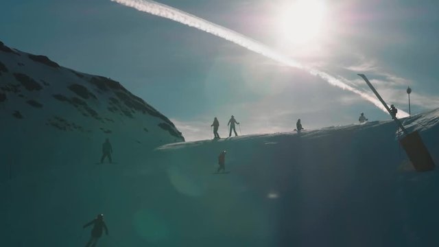 Skiers on mountain pass travelling down hill slow motion.