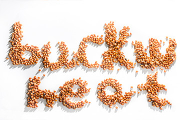 Inscription of the words buckwheat with buckwheat grains on a white background, texture