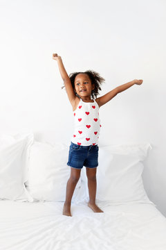 Girl standing on bed holding her arms up