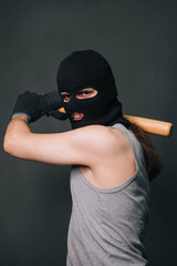 Bandit, the criminal in a black mask and in a gray T-shirt with a painless bat. Robber with a weapon. A man in a balaclava and a gray mask on a gray background