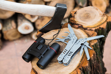 axe, binoculars and multitool knife case on the stump, firewoods on the background