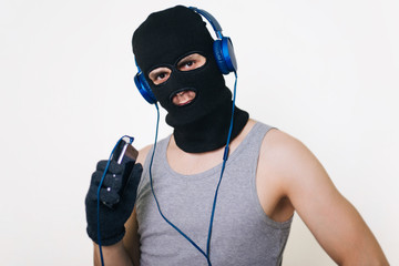 A man in a balaclava with a cell phone and headphones. the criminal downloads music is not legal. theft of music.