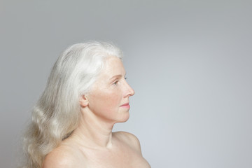 Side view of a mature woman with shiny long white hair, but without make-up, gray background, copy space.