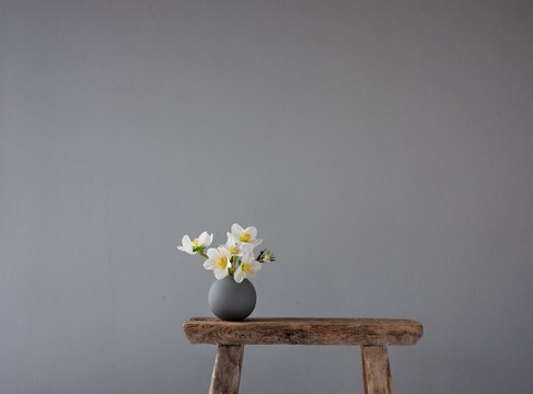 Runde, graue Vase mit Frühlingsblumen auf altem Holzhocker