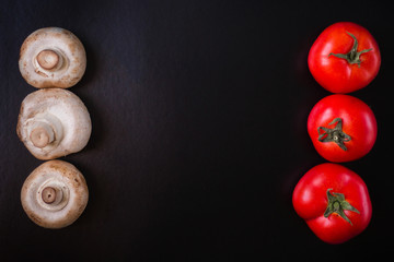 Mushrooms champignons with red tomatoes on a black background