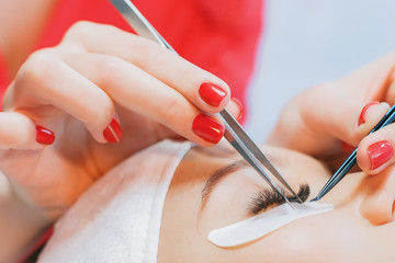 Eyelash Extension Procedure. Woman Eye with Long Eyelashes. Beautiful young girl  tweezing her eyebrows in a beauty salon. Eyebrow Correction. Beauty Concept. Permanent Makeup. Microblading brow.