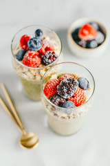 Top view on portions of chia pudding with matcha tea, organic granola, frozen berries in glasses. The concept of healthy vegan food.
