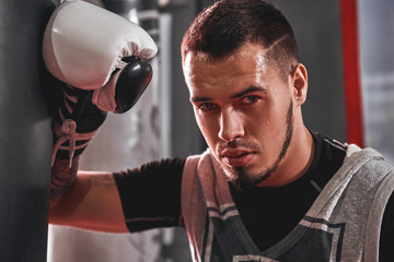 Tired after workout. Tired young athlete in sports clothing looking away after hard training on heavy punch bag in boxing gym